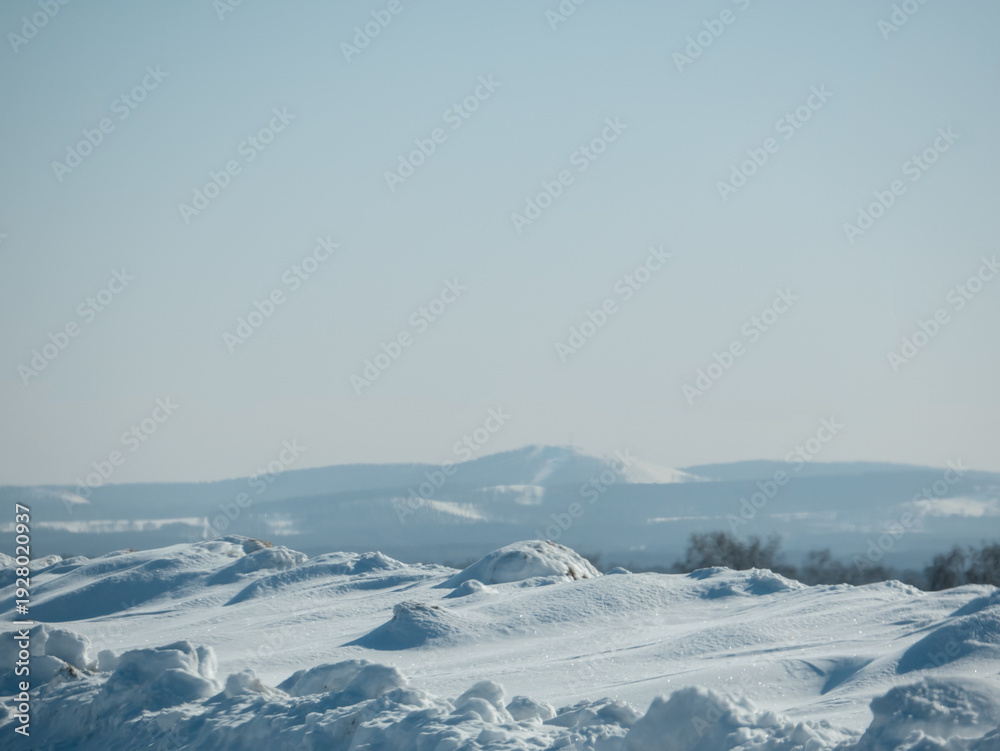 Obraz premium Winter landscape with snowdrifts and distant hills under a clear blue sky. Cold season scenery for nature background or greeting card.