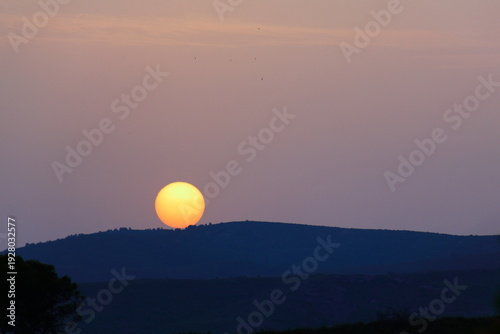 Golden Sun Setting Over Rolling Hills at Tranquil Purple-Orange Sunset Horizon