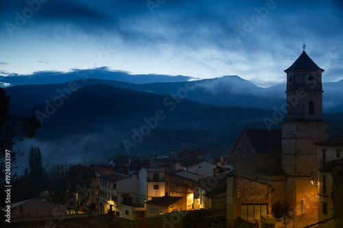 Misty Mountain Village of Casas Altas in Valencia (Spain) at Dawn With Historic Church Tower and Warm Street Lights in Twilight