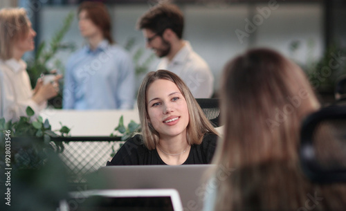 A woman is sitting at a desk with a laptop and smiling
