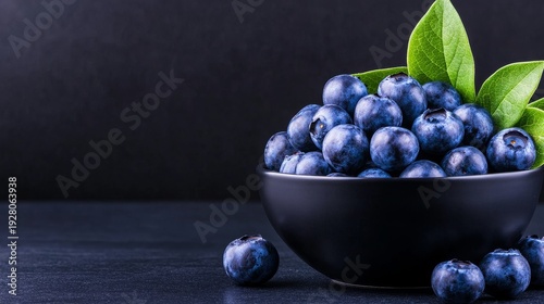 A close-up of fresh blueberries in a black bowl, surrounded by lush green leaves, on a dark surface