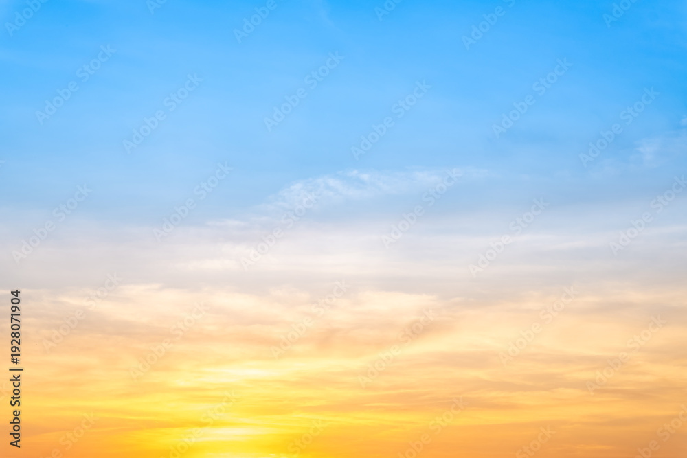 Obraz premium Beautiful sunrise sky with vibrant gradient orange and gold colors and soft blue, Clear atmosphere with wispy clouds. Peaceful, perfect for background and copy space, High resolution images