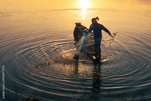 Quadro su tela Male fisherman on boat throwing fishing net in the lake during sunset