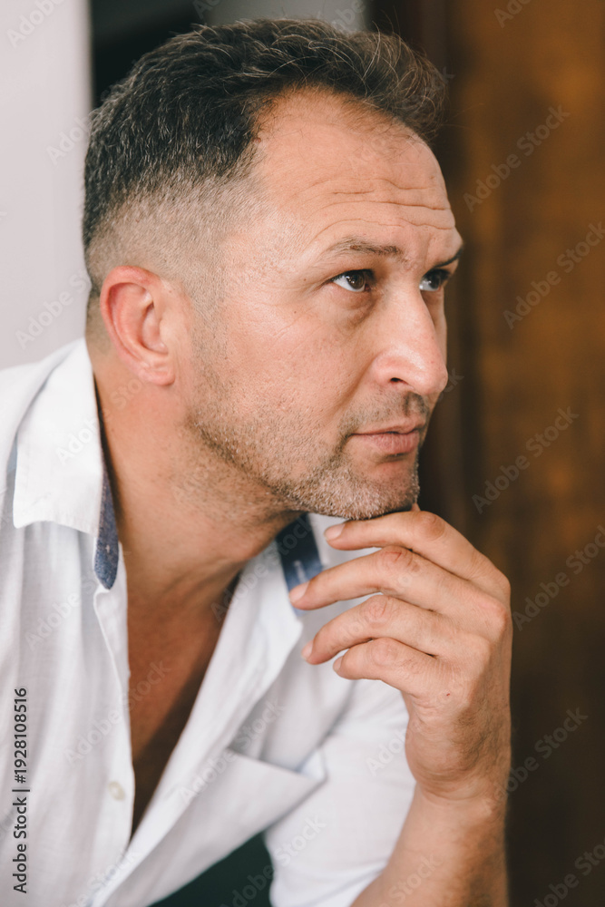 Fototapeta premium Indoor side-profile portrait of a thoughtful mature man, captured in soft natural light with a calm, reflective mood.