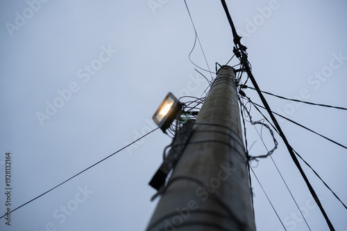 Concrete utility pole with glowing lamp and black cables