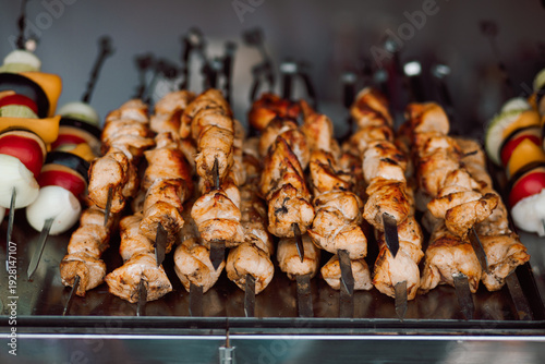 Photos Grilled chicken, beef or pork meat skewers shish kebab shashlik cooking on a metal grill, surrounded by colorful vegetables like onions, peppers, and tomatoes