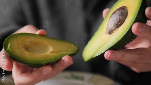 avocado halves being held open to reveal the pit and green flesh. A professional culinary shot showcasing the buttery texture and vibrant color of a ripe Hass avocado, ideal for healthy eating