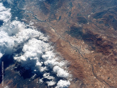 Aerial shot reveals a vast, rugged landscape with a meandering river, fluffy clouds, and varying terrains