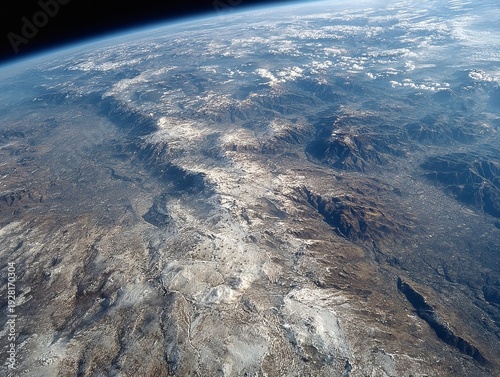Aerial view from space showcasing a mountainous landmass, partly covered in snow, with atmospheric haze and clouds