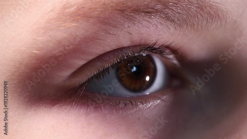 Extreme macro close-up of a young boy's brown eye looking into the distance and blinking calmly.