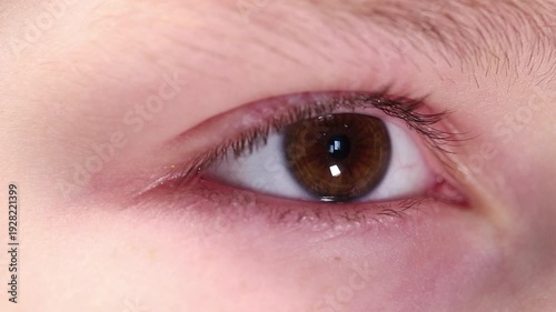 Extreme macro close-up of a young boy's brown eye looking into the distance and blinking calmly.