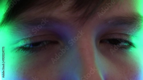 Extreme macro of a young boy's eyes reflecting colorful running neon lights in the dark