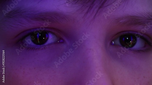 Extreme macro of a young boy's eyes reflecting colorful running neon lights in the dark