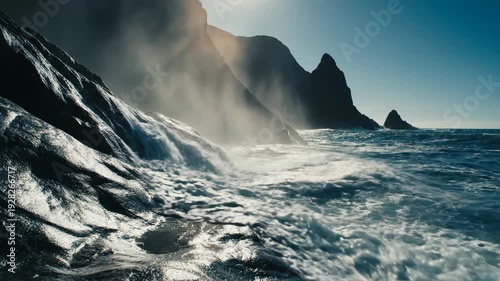 Dramatic ocean waves crash against rugged rocky coastline with misty atmosphere