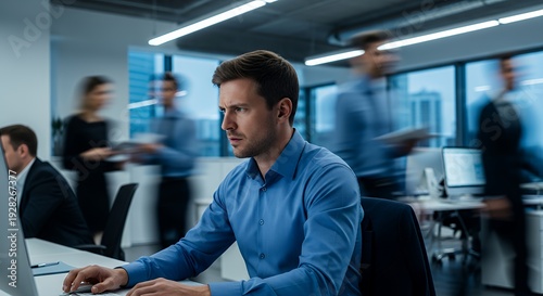 high quality, sharp focus, detailed, man sitting at desk, working on laptop, office setting with people in background, focused expression, blue shirt, professional
