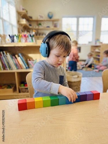 Autism Spectrum: Professional photography, a child wearing noise-canceling headphones in a bright classroom, stacking toys in a perfect line, soft focus background, authentic.