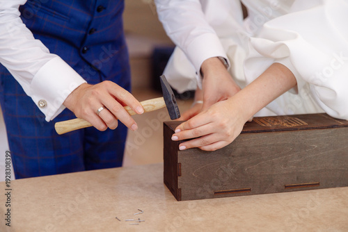 фотографія Close-up of newlyweds using a hammer to seal a wooden box during a wedding tradi