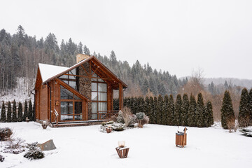 Modern wooden lodge nestled in a snowy pine forest during winter snowfall