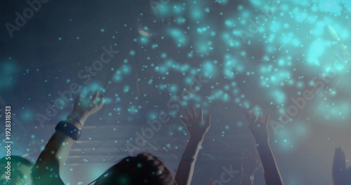 Reaching crowd raising hands toward teal-blue lights at nightclub, with truss, wristbands, haze