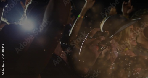 Holding smartphone, hands recording concert at venue, showing camera flashes, brimmed hat, haze