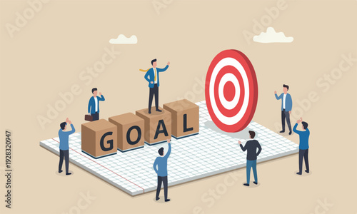 Business businessman leader standing on wooden stamp with alphabet building the word GOAL on graph paper notebook with other people admiring