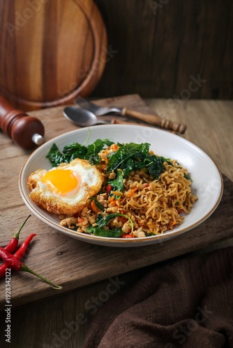 Fotografie Spicy Thai Stir-fried Instant Noodles (Mama Pad Kra Pao) with Minced Pork, Holy Basil, and a Crispy Fried Egg on a Rustic Wooden Table