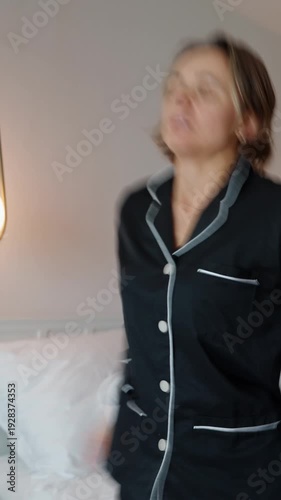 Woman standing in a modern hotel room after waking up, holding her head as she experiences dizziness. Wearing pajamas, she appears disoriented and slightly unwell, suggesting fatigue, jet lag