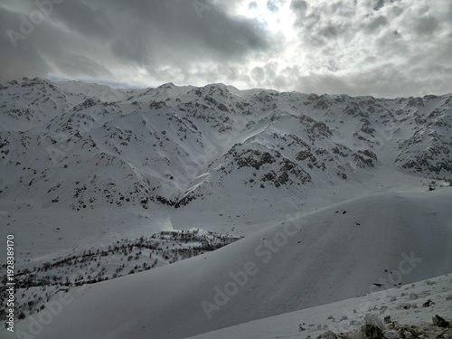 Canvas Print Snow-covered mountain ranges under soft winter light, with drifting clouds highlighting the rugged alpine slopes and expansive untouched terrain