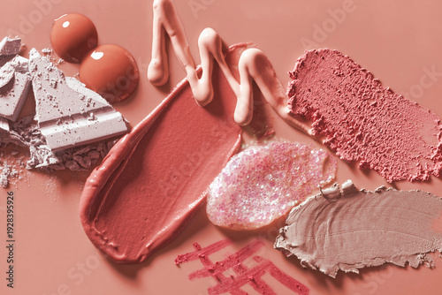 Composition of various makeup textures: creamy lipstick, liquid foundation, shimmering gloss, and crushed powder on a dusty rose background