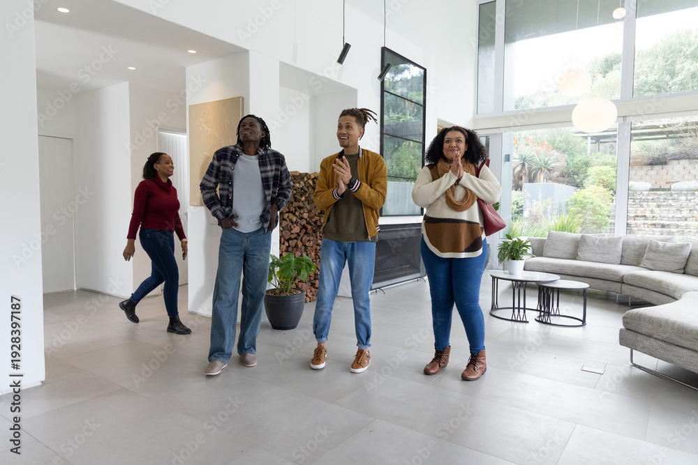 Fototapeta premium African American friends walking into modern living room, clapping near fireplace and windows