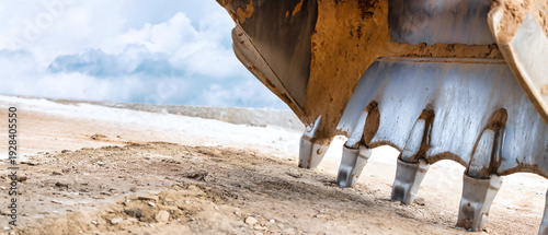 Obraz na plátně A powerful excavator bucket breaks ground on a sunlit day, sending dirt flying a