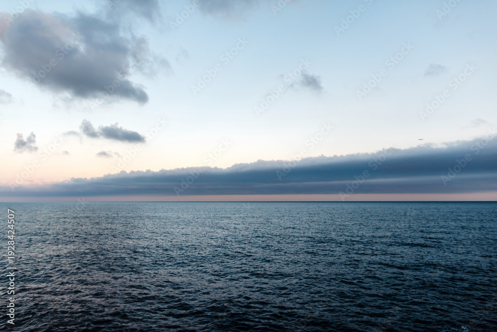 Fototapeta premium Barcelona's vast ocean horizon under a dramatic sky with distant airplane