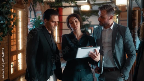 Real estate agent presenting property details on tablet to investors or buyer before touring luxury hotel interior. Business inspection and investment consultation.