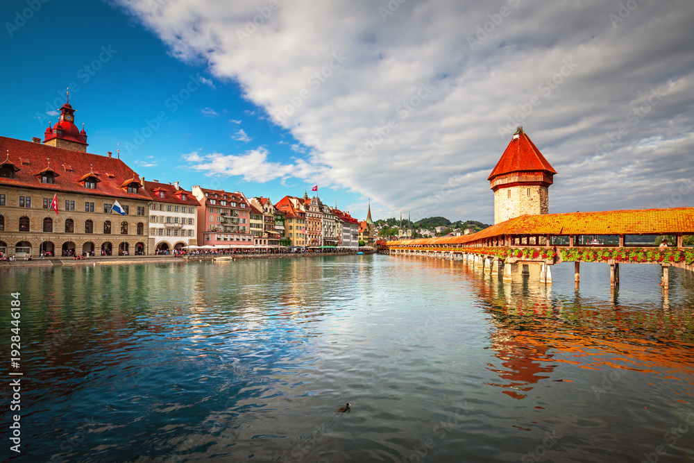 Obraz premium Beautiful view of Lucerne, Switzerland featuring the famous wooden Chapel Bridge with Water Tower over the Reuss River. Scenic cityscape with alpine mountains, clear water, and colorful historic archi