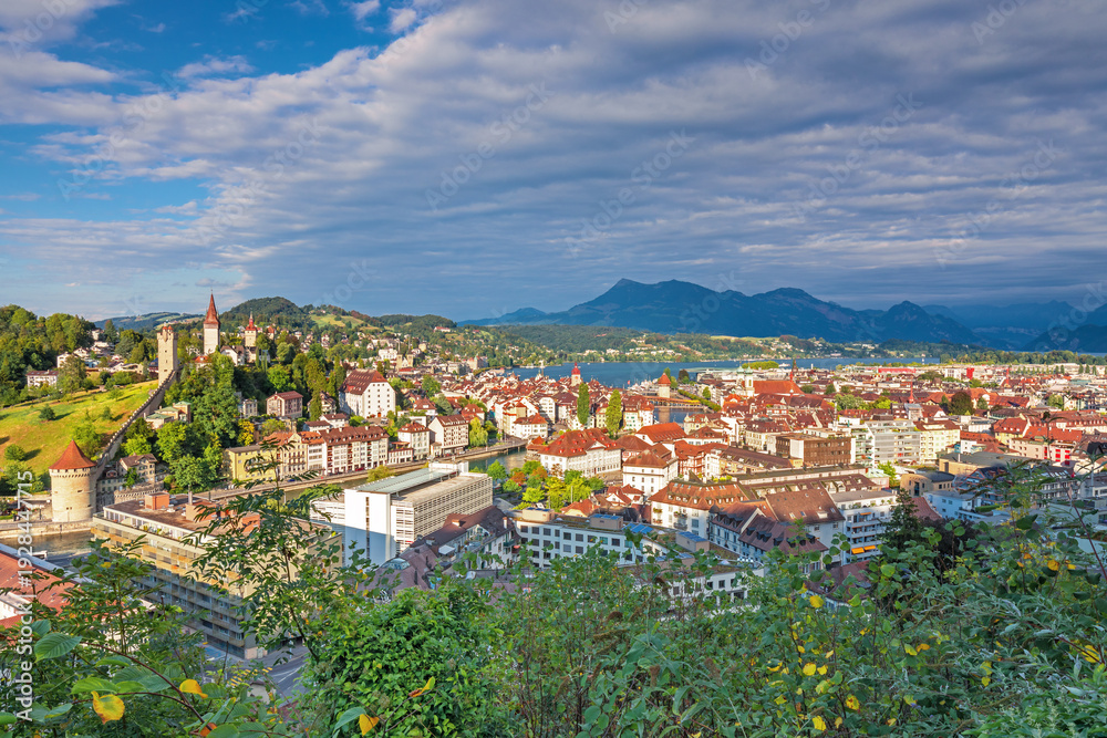 Obraz premium Beautiful view of Lucerne, Switzerland featuring the famous wooden Chapel Bridge with Water Tower over the Reuss River. Scenic cityscape with alpine mountains, clear water, and colorful historic archi