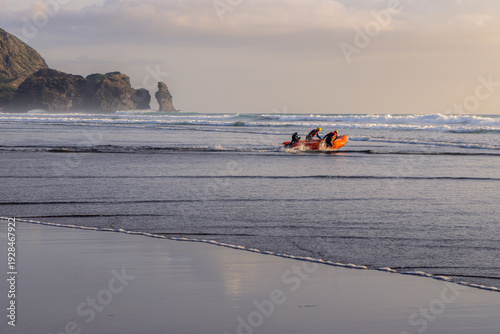 Fotografie Lifeguards in an IRB (inflatable rescue boat) patrol the surf at Piha Beach, Auckland, New Zealand, ensuring swimmer safety and responding to emergencies