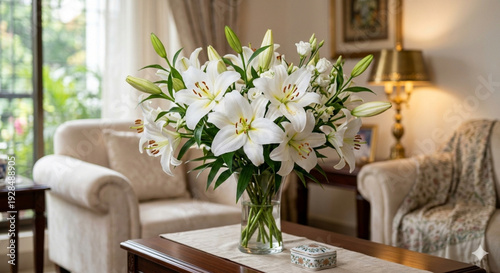 Elegant bouquet of white lilies in a glass vase on a wooden table in a tastefully decorated living room with soft natural light