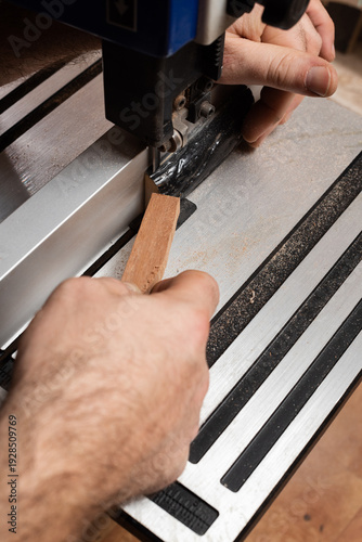 A craftsman saws off a piece of horn to make a nut for a stringed instrument, using a stick to help push the piece through