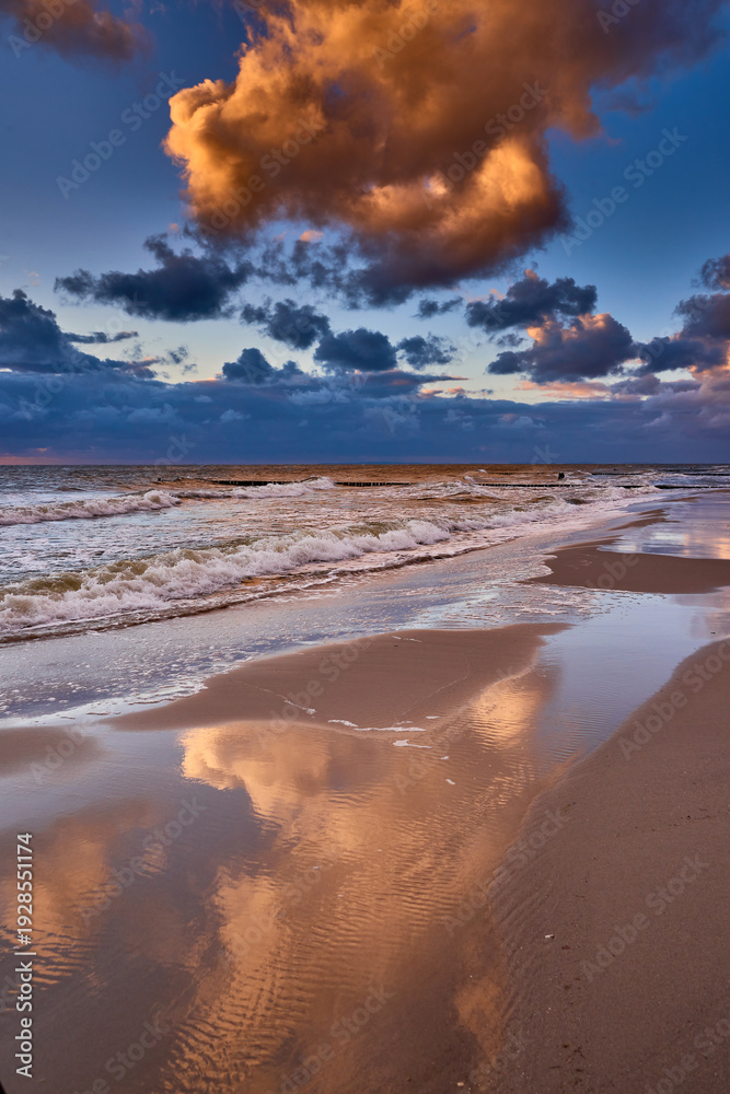 Fototapeta premium Dramatic Sunset Sky Reflected on Wet Beach Sand with Ocean Waves and Groynes