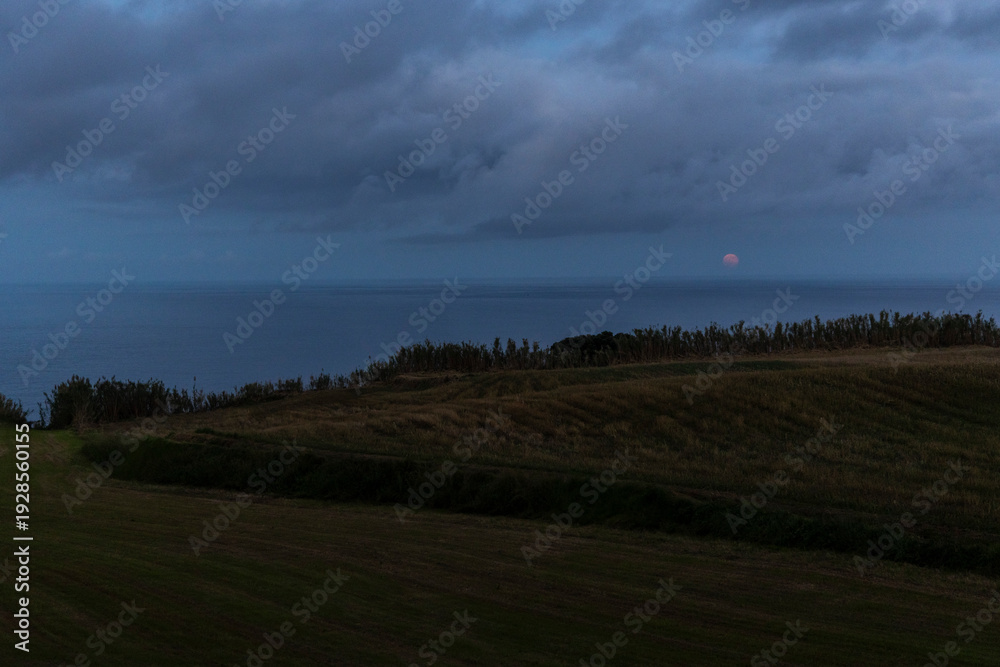 Fototapeta premium A cloudy sky with a red full moon in the background above the sea.