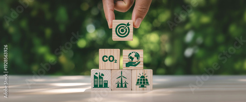 Hand holding wooden blocks with environmental icons representing sustainability and carbon reduction goals