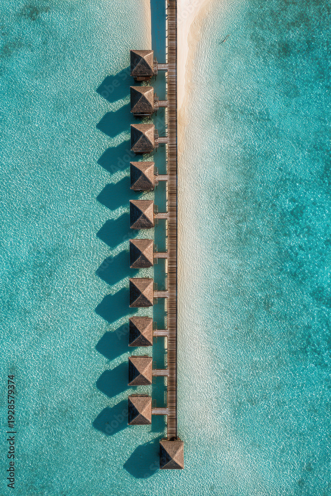Fototapeta premium Overhead drone view of tropical luxury overwater villas connected by wooden pier above crystal clear turquoise lagoon, aerial top down perspective of exotic island resort