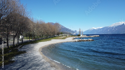 Pebble beach in Toscolano Maderno with snowy mountains and Lake Garda, Italy