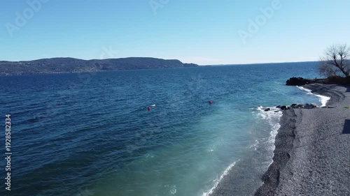 Pebble beach in Toscolano Maderno with snowy mountains and Lake Garda, Italy