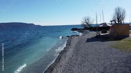 Pebble beach in Toscolano Maderno with snowy mountains and Lake Garda, Italy