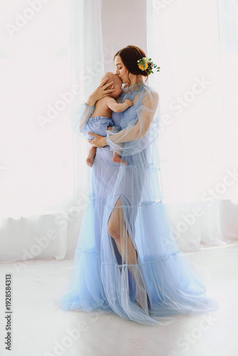 Mother kissing baby in tender moment, woman in soft blue tulle dress, emotional motherhood bonding portrait
