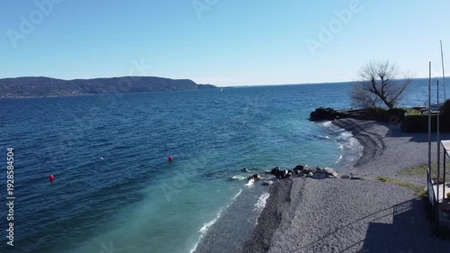 Pebble beach in Toscolano Maderno with snowy mountains and Lake Garda, Italy