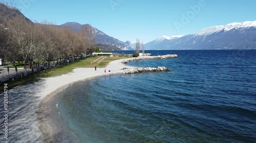 Pebble beach in Toscolano Maderno with snowy mountains and Lake Garda, Italy