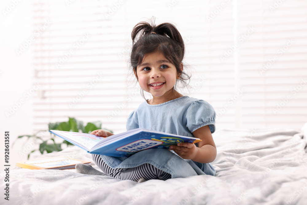 Naklejka premium Cute little girl reading book on bed at home