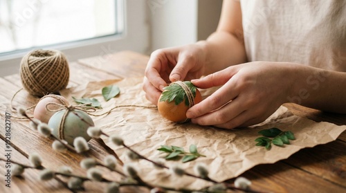 Woman decorating Easter eggs with natural leaves and twine at a wooden table, spring crafts, holiday preparation, DIY tradition, creative family activity, Easter.